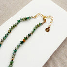 Necklace with small green agate and gold beads on a white surface