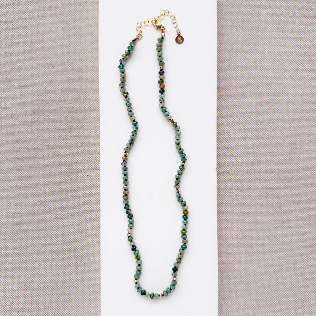 Necklace with small green agate and gold beads on a white surface