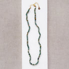 Necklace with small green agate and gold beads on a white surface