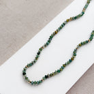 Necklace with small green agate and gold beads on a white surface