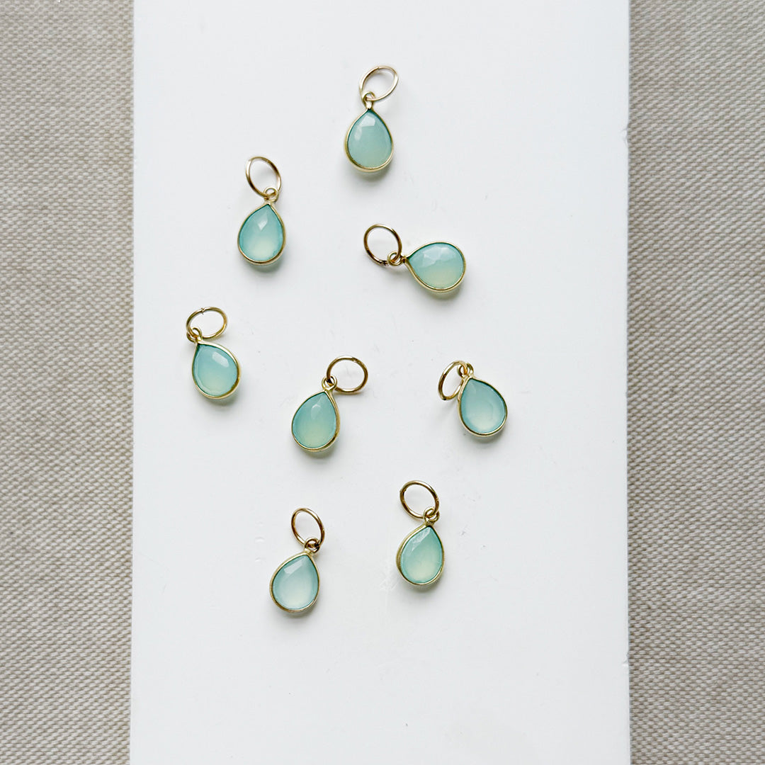 Teardrop shaped aqua chalcedony charms on a white plate