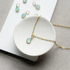 Teardrop shaped aqua chalcedony charm on a gold chain in a white dish