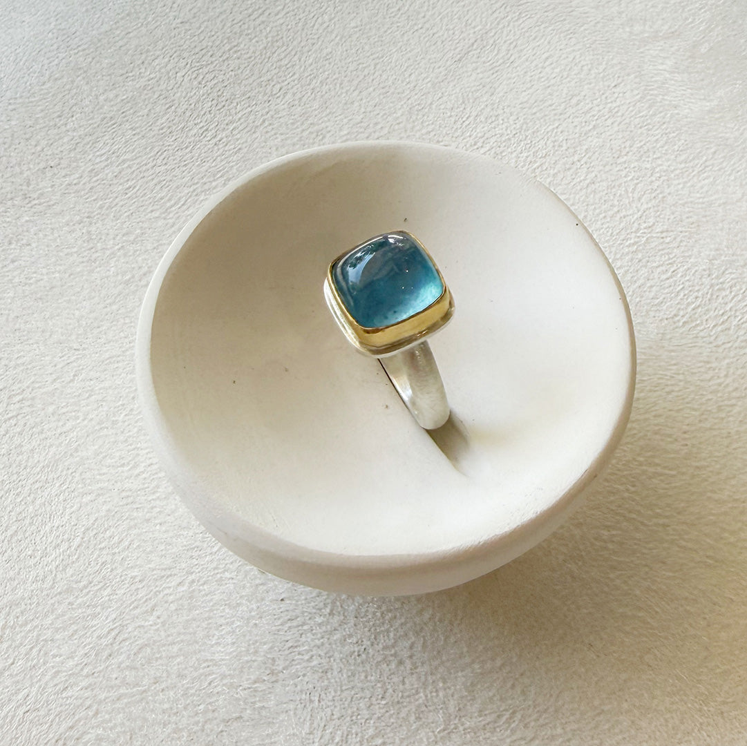 Smooth cushion cut mixed metal aquamarine ring in a white dish