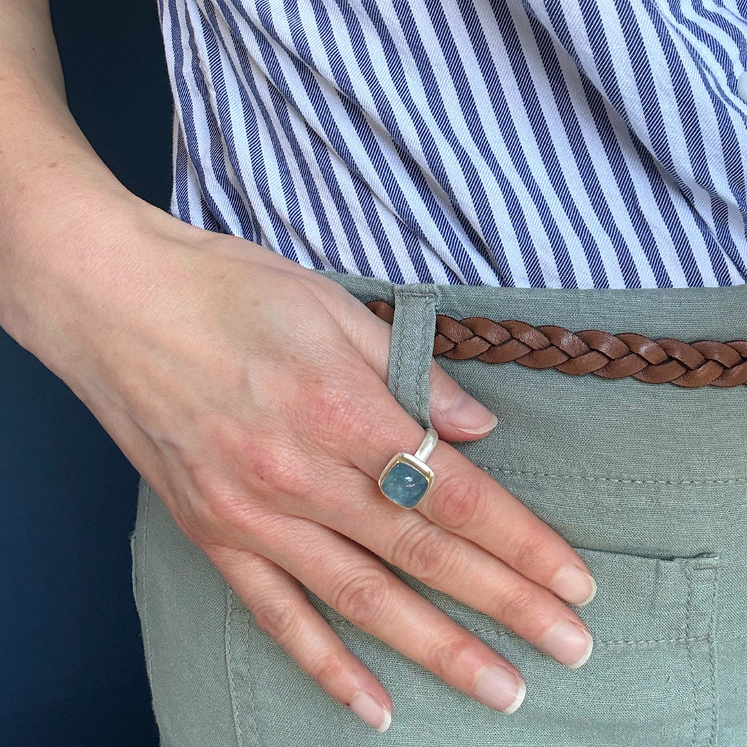 Hand wearing a smooth cushion cut mixed metal aquamarine ring 