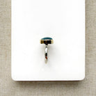 A silver ring with a small oval aquamarine cabochon gemstone, displayed on a white rectangular card over a beige woven fabric background.