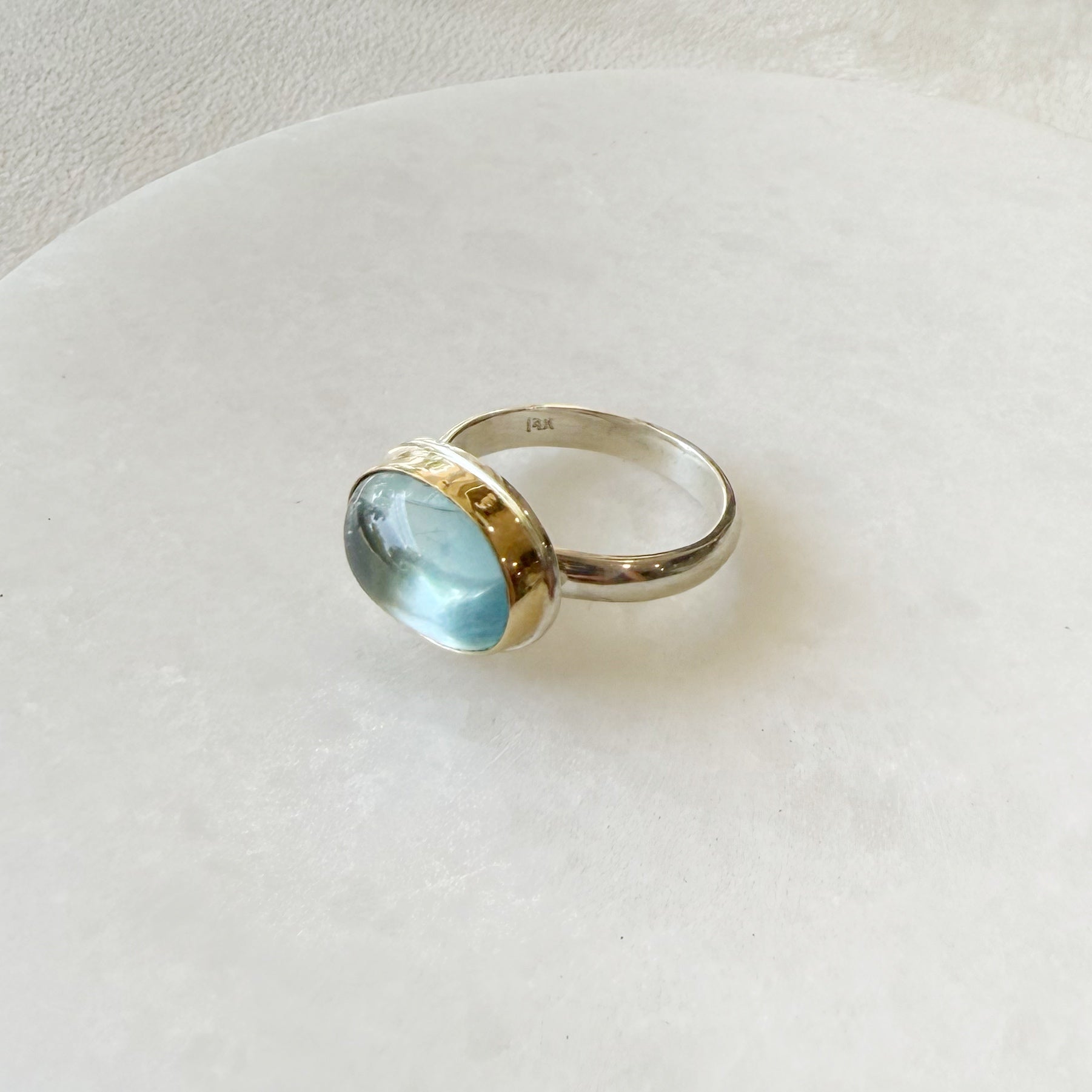 Oval aquamarine mixed metal ring on a white dish 