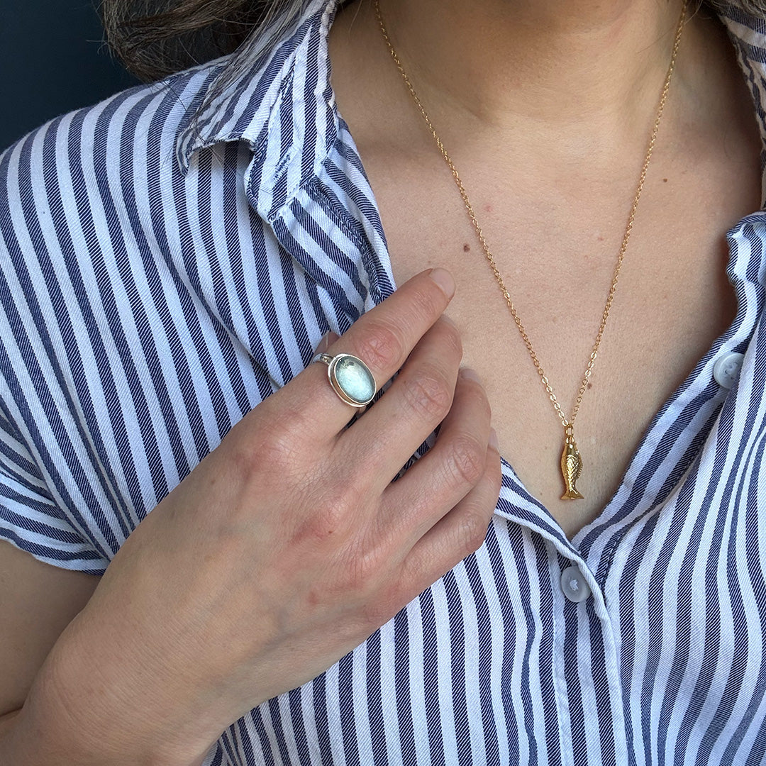 Close up of woman wearing an oval aquamarine mixed metal ring and a gold fish pendant