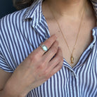 Close up of woman wearing an oval aquamarine mixed metal ring and a gold fish pendant