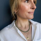 Person wearing a green kyanite gemstone necklace and gold pendant with a white shirt.