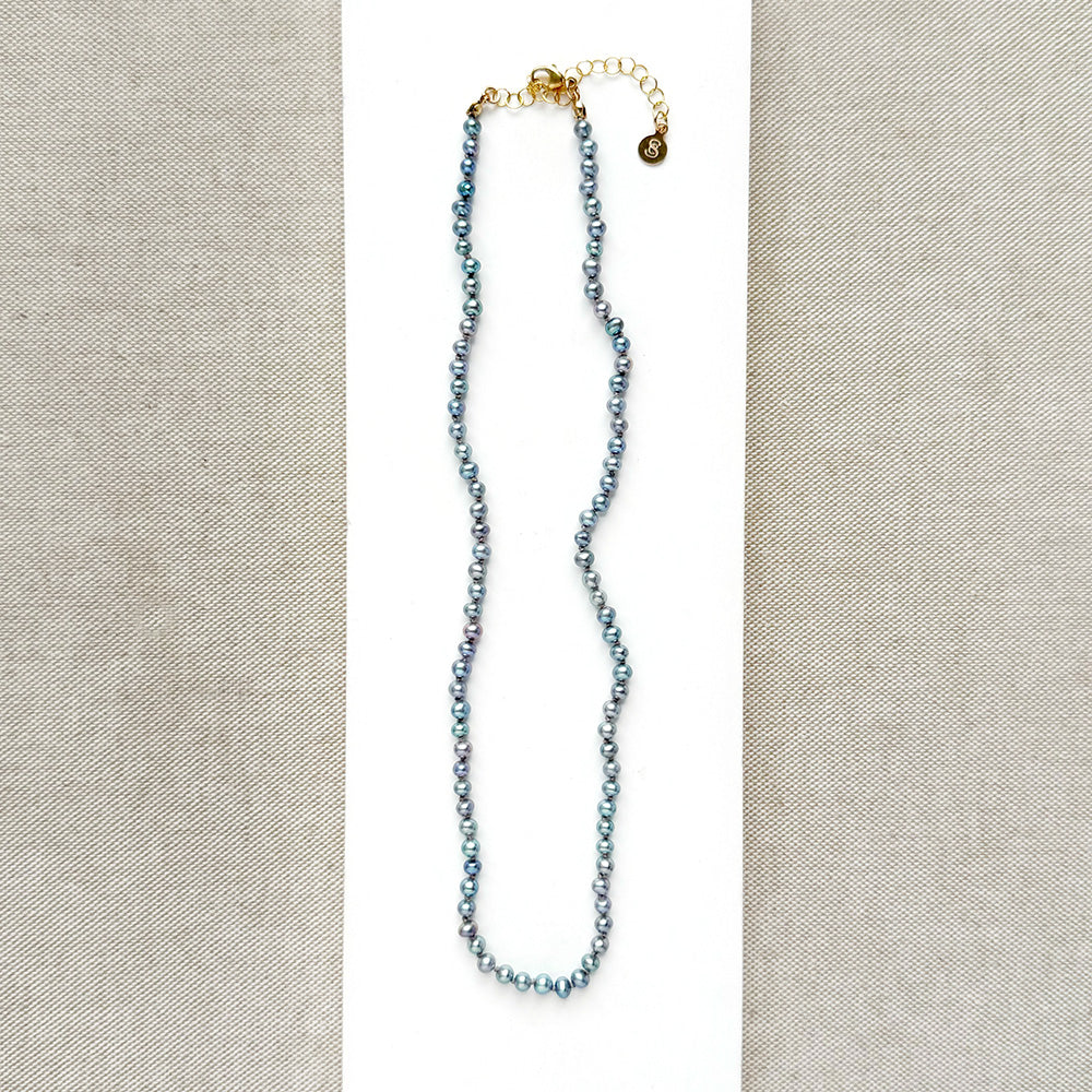 Knotted necklace with small round peacock pearls on a white dish