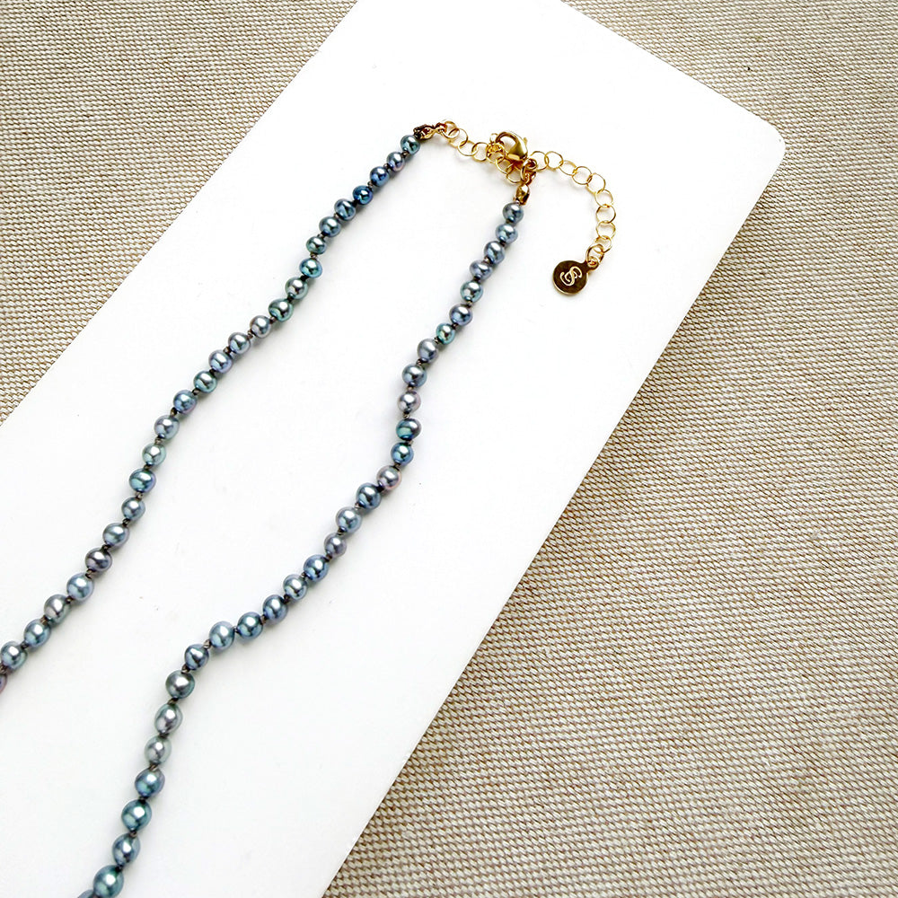 Knotted necklace with small round peacock pearls on a white dish