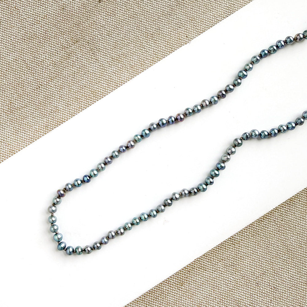 Knotted necklace with small round peacock pearls on a white dish