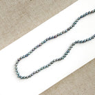 Knotted necklace with small round peacock pearls on a white dish