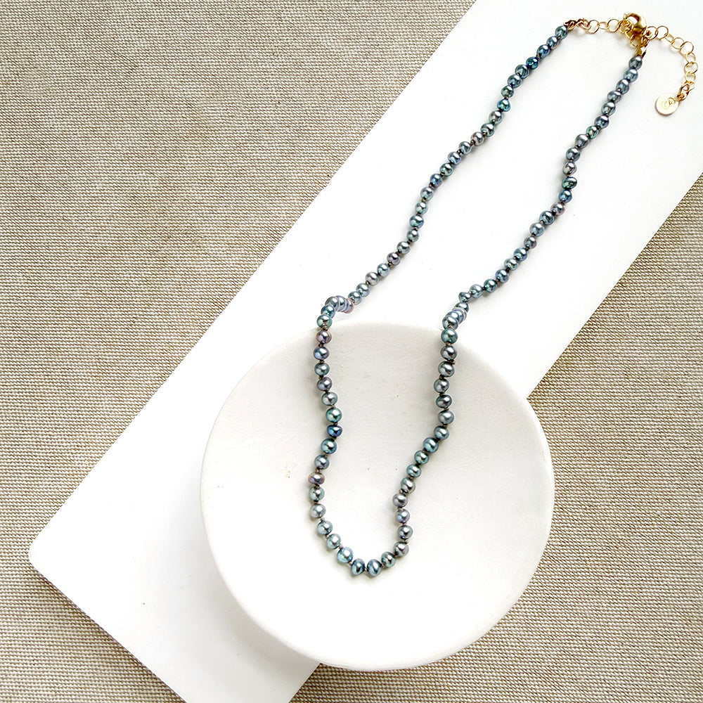Knotted necklace with small round peacock pearls in a white dish