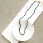 Knotted necklace with small round peacock pearls in a white dish