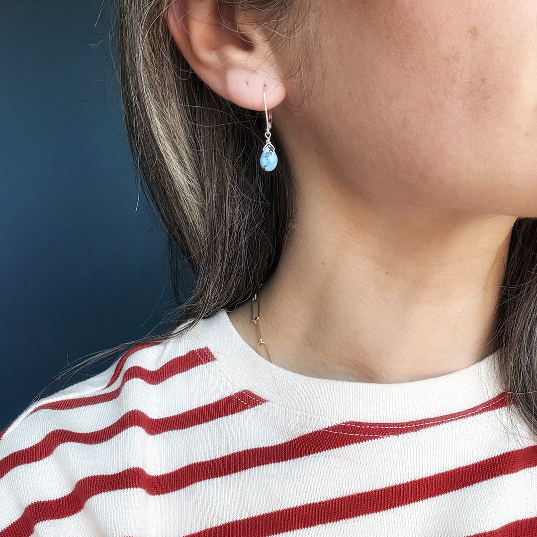 Close up of woman wearing tear drop shaped Golden Hills turquoise earrings in silver