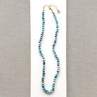 A knotted Golden Hills turquoise necklace, draped over a white plate on a neutral textured surface.
