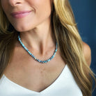 A close-up of a woman wearing a knotted Golden Hills turquoise necklace, paired with a white top against a dark blue background.