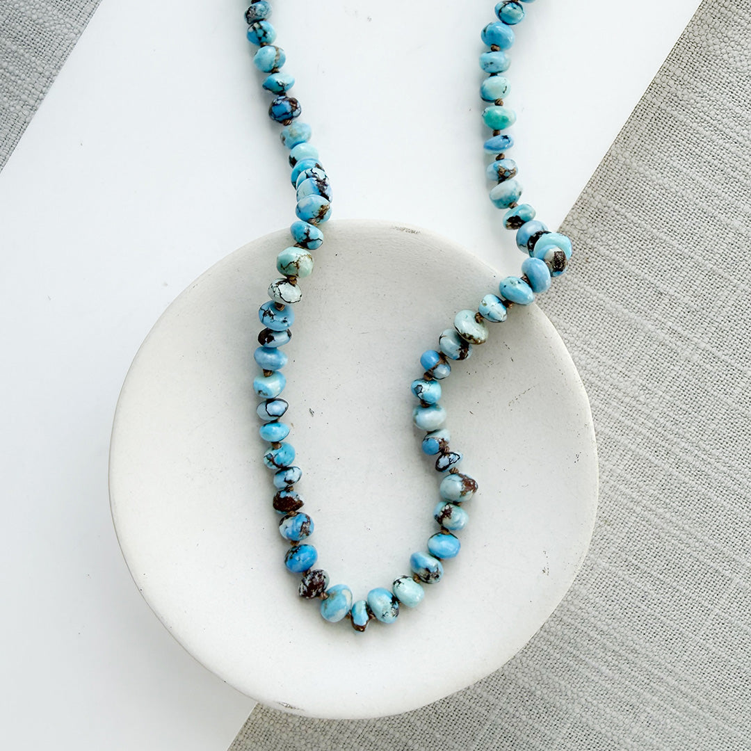 Necklace with Golden Hills turquoise beads on a white dish against a gray background