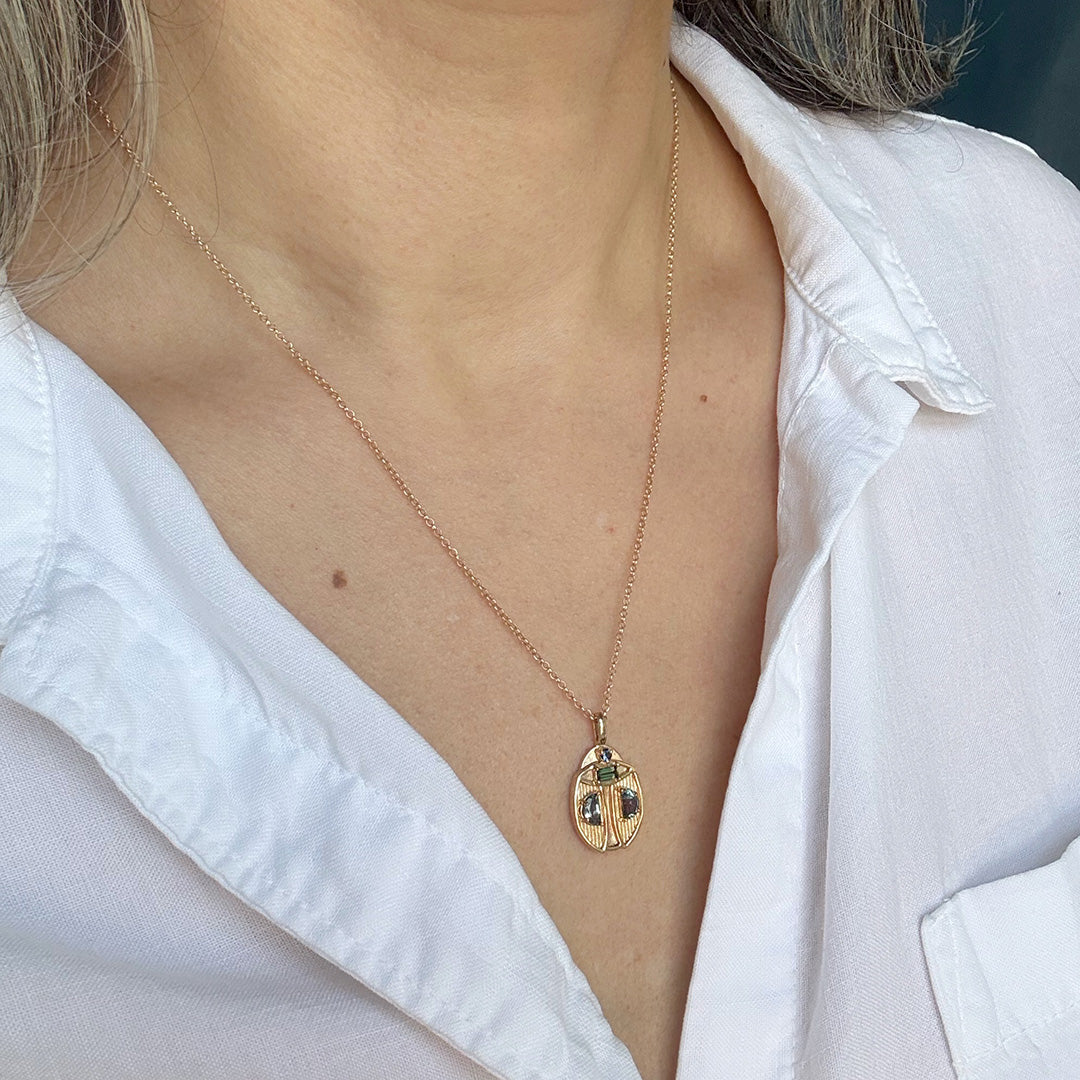 Gold beetle necklace with a pendant worn by a person in a white shirt.