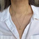 Person wearing a gold beetle necklace with a pendant against a white shirt background