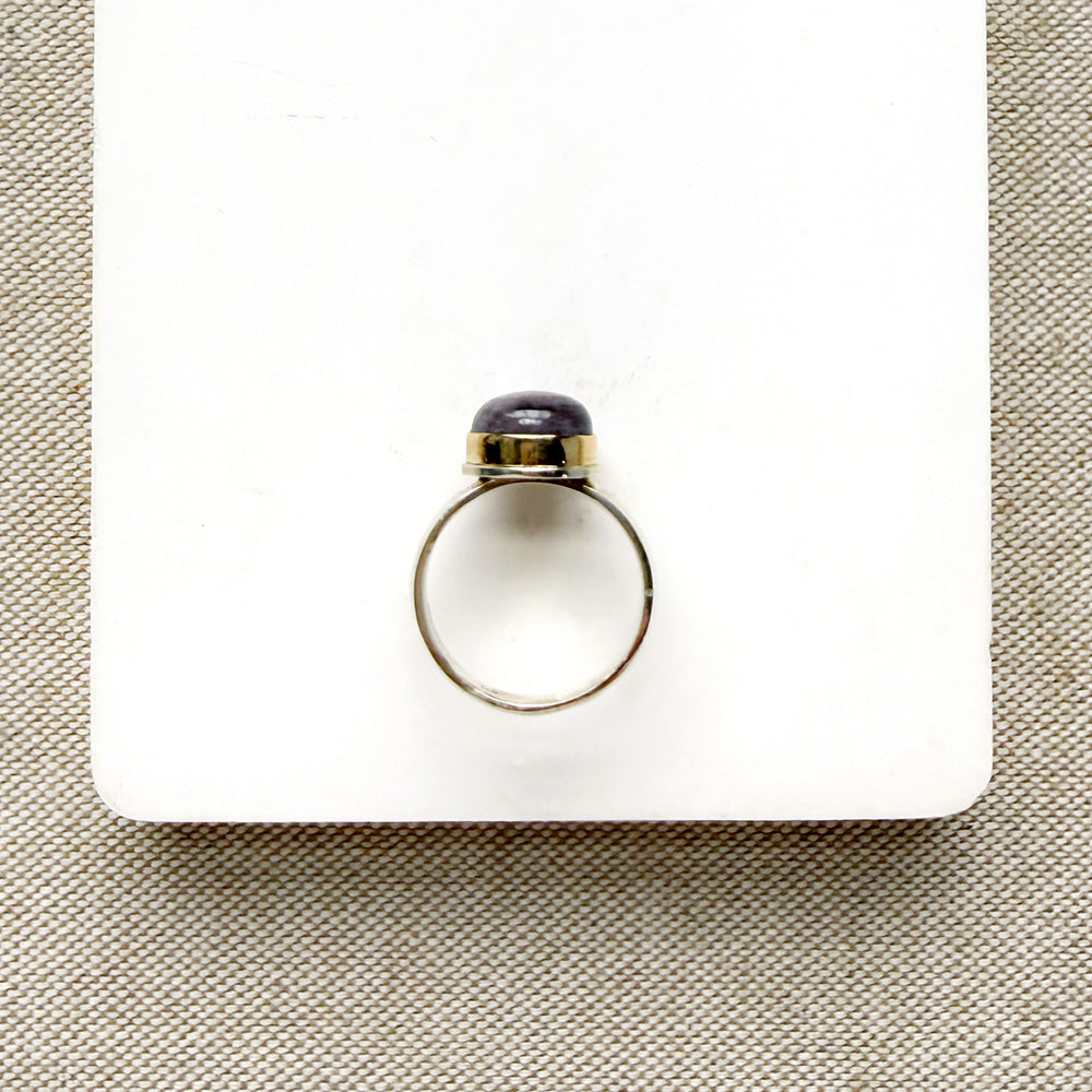 Side view of round berry spinel ring in a mixed metal setting, placed on a white dish