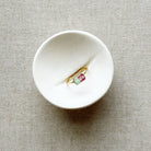 Gold ring with a green gemstone in a white dish on a beige fabric background