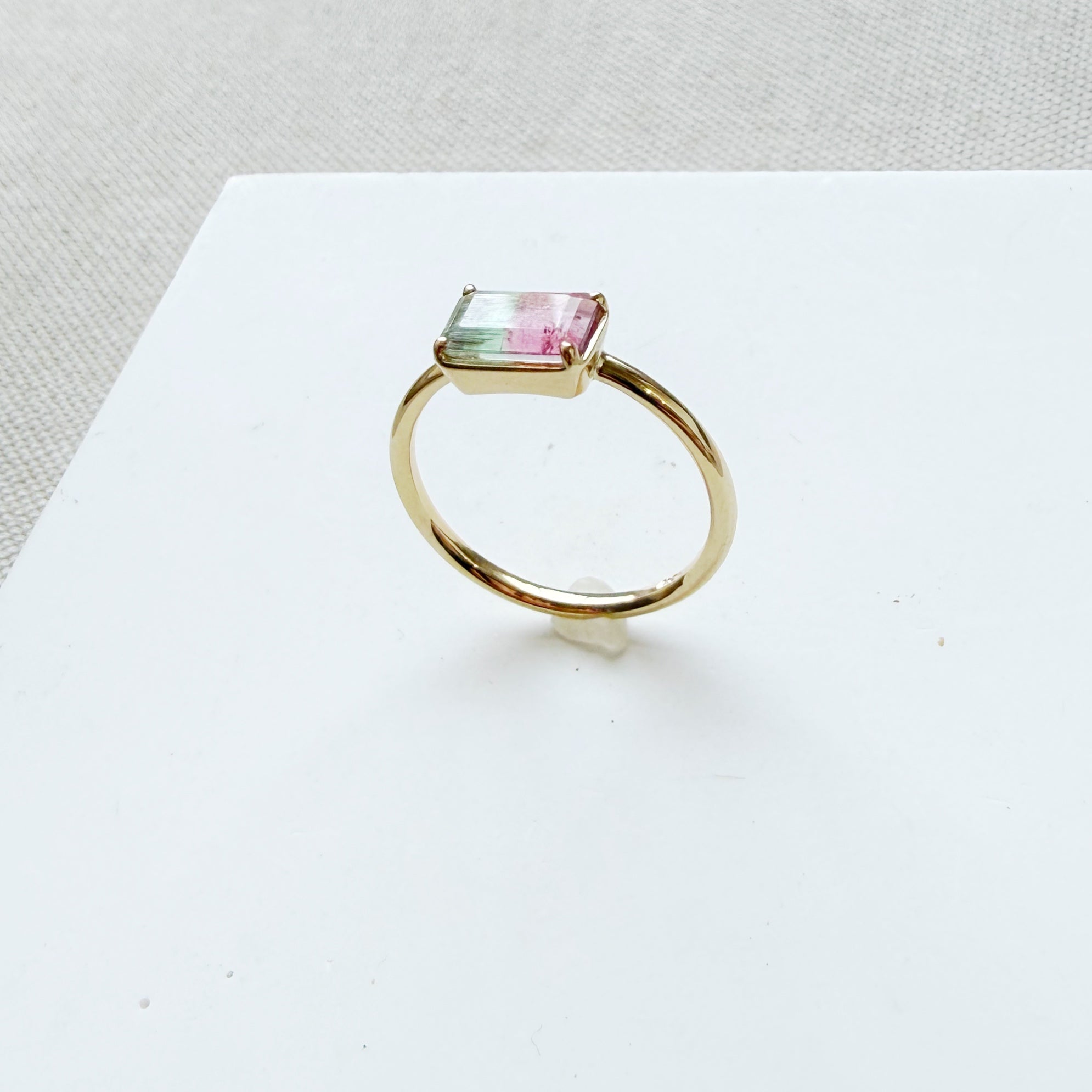 Gold ring with a pink and green gemstone on a white surface