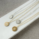 Four necklaces with circular pendants featuring engraved flower designs on a white surface.
