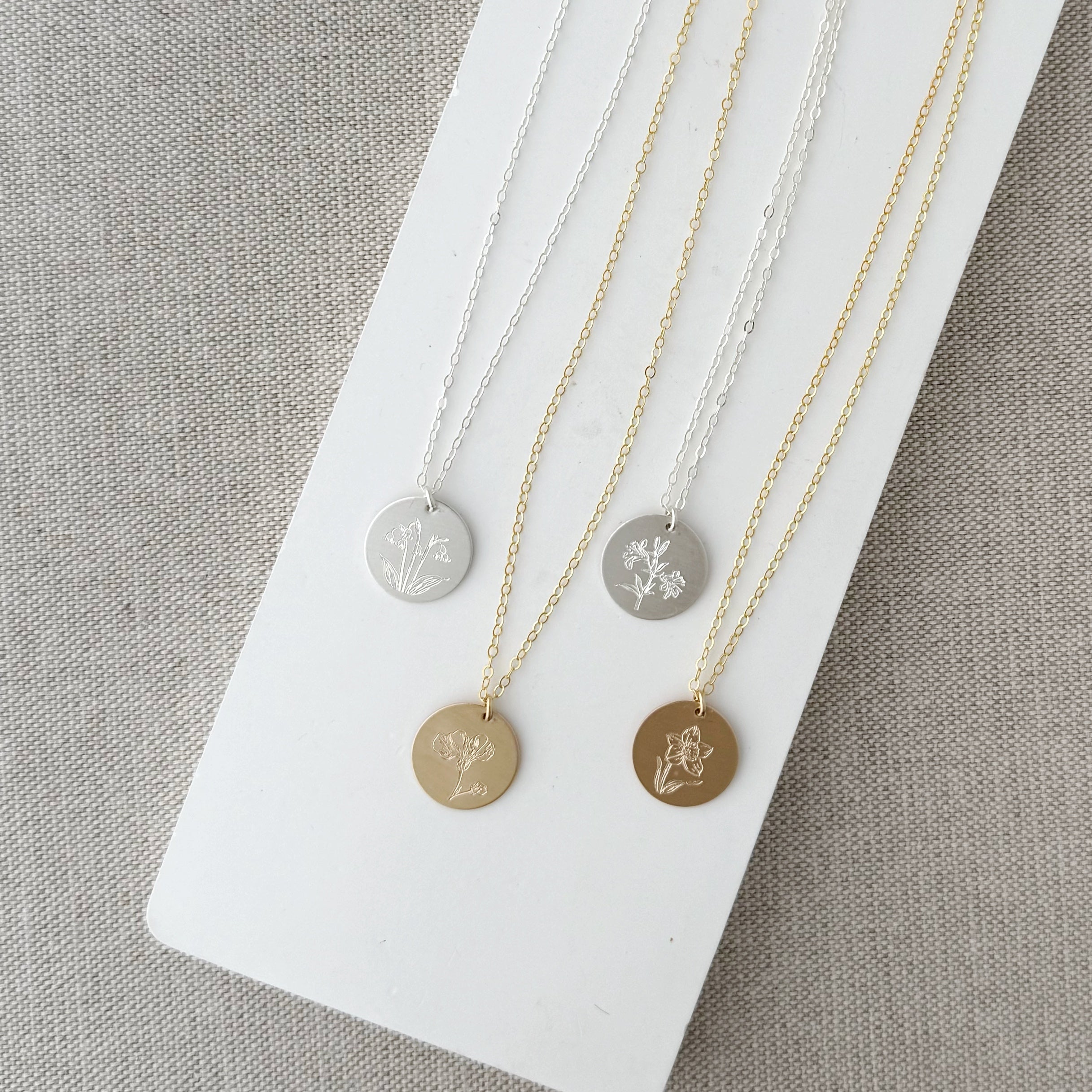 Four necklaces with circular pendants featuring engraved flower designs on a white surface.