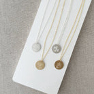 Four necklaces with circular pendants featuring engraved flower designs on a white surface.