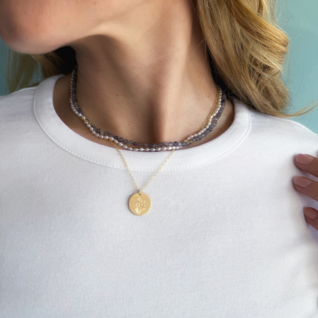 Close-up of a person wearing a gold pendant necklace with an engraved flower on a white shirt with a light blue background