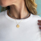 Close-up of a person wearing a gold pendant necklace with an engraved flower on a white shirt with a light blue background