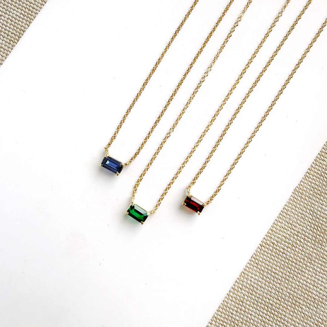 Three gold necklaces with colored gemstones on a white background