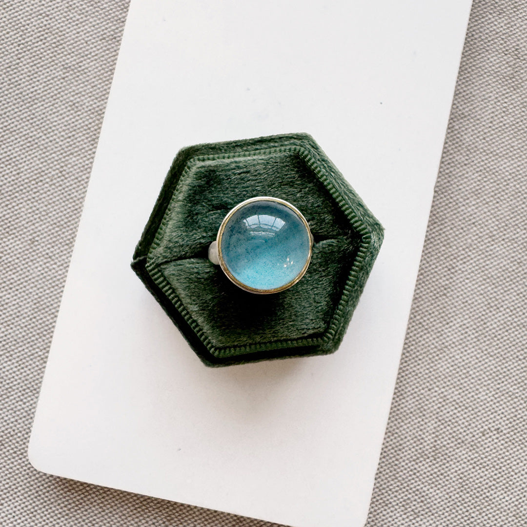 Ring with a round blue aquamarine gemstone in a green hexagonal box on a white surface