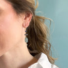 Woman wearing a gemstone statement earring and a white shirt with a light blue background