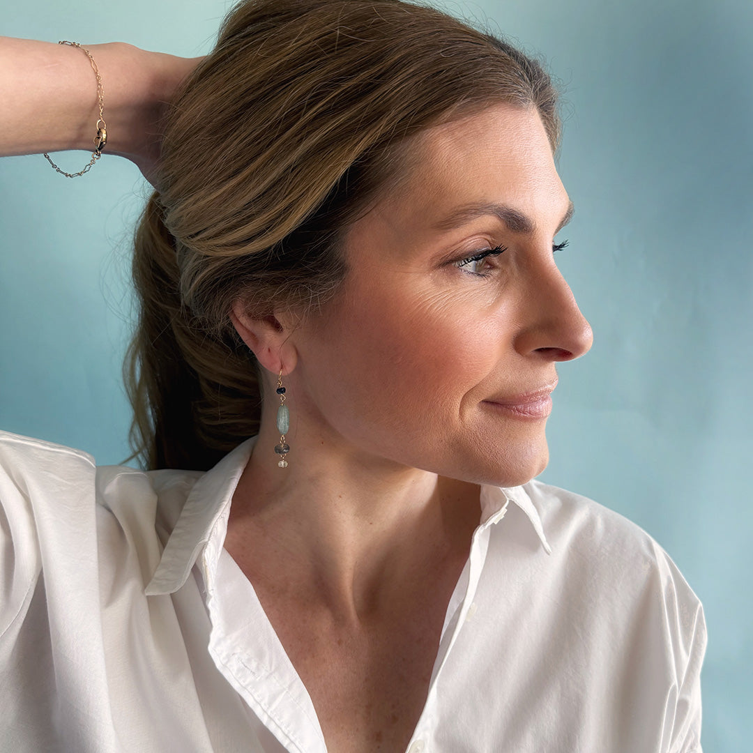 Woman wearing a gemstone statement earring and a white shirt with a light blue background