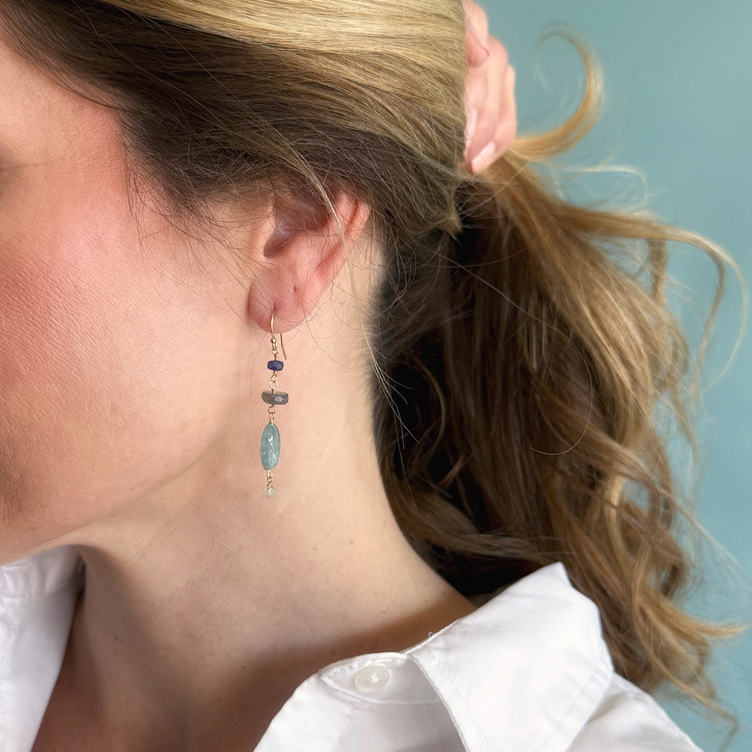 Woman wearing a gemstone statement earring and a white shirt with a light blue background