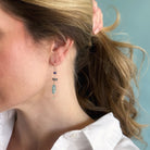 Woman wearing a gemstone statement earring and a white shirt with a light blue background