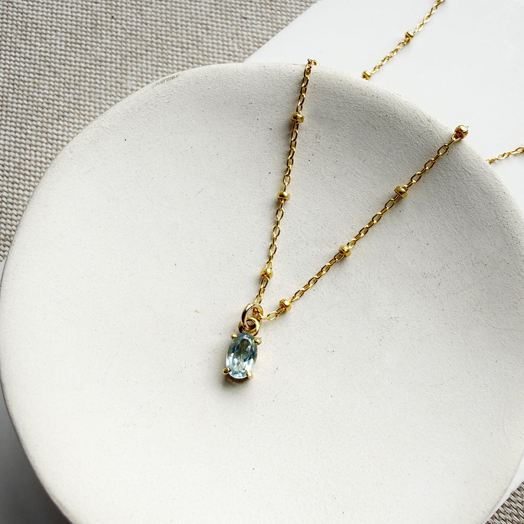 Blue gemstone pendant on a gold chain in a white dish