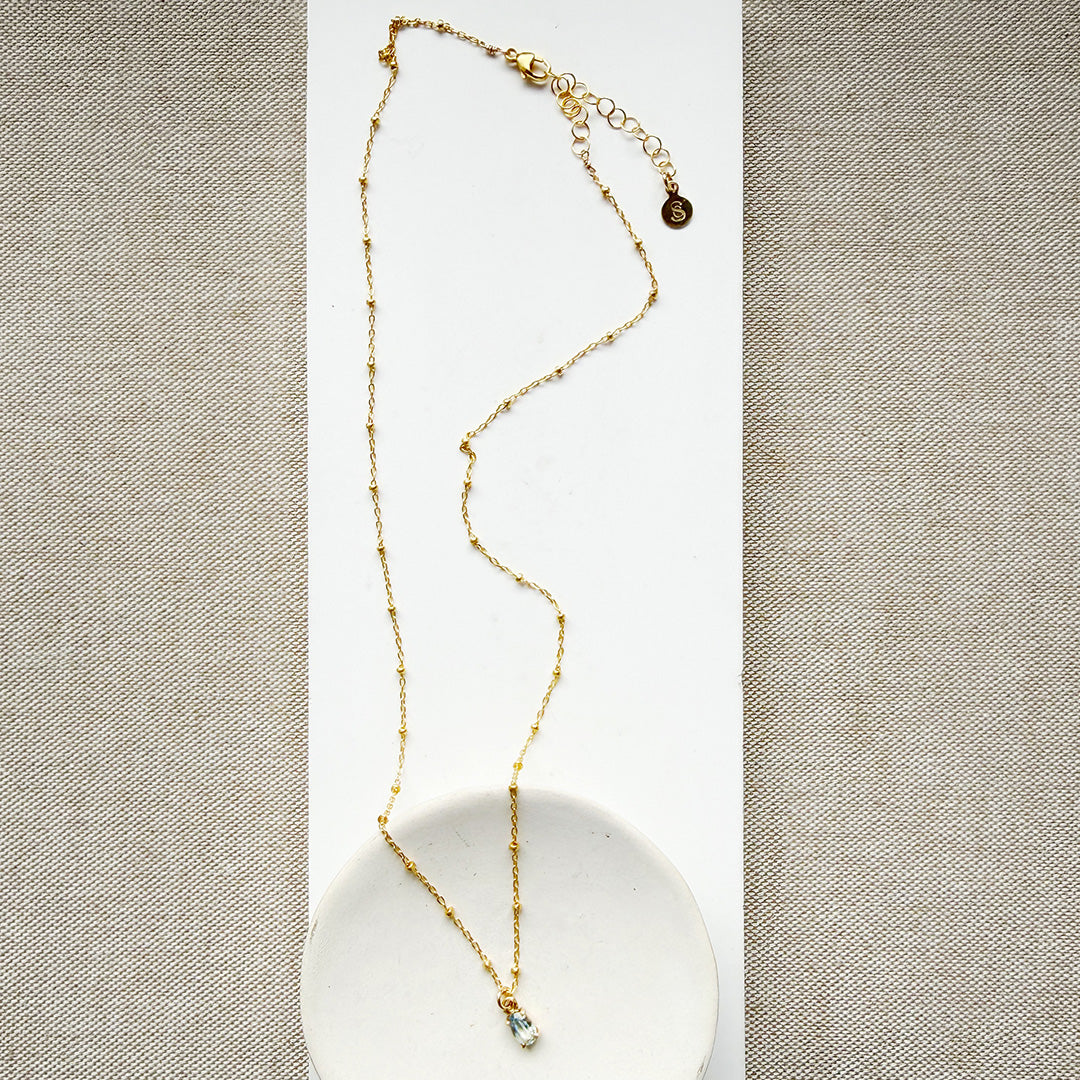 Blue gemstone pendant on a gold chain in a white dish