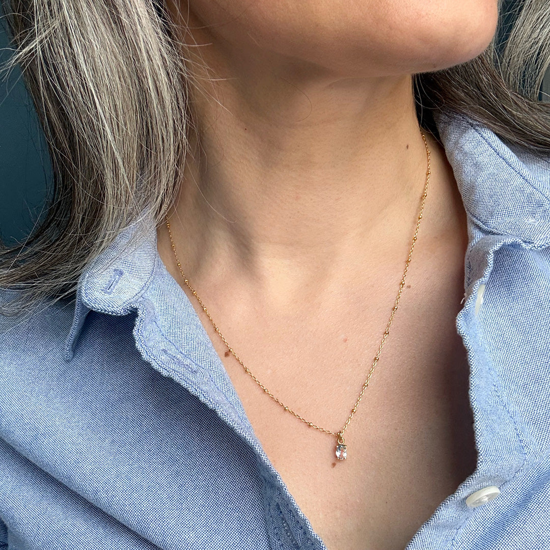 Gold necklace with a small blue gemstone pendant worn by a person in a blue shirt.