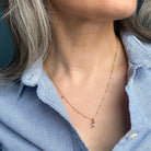 Gold necklace with a small blue gemstone pendant worn by a person in a blue shirt.
