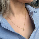 Gold necklace with a small blue gemstone pendant worn by a person in a blue shirt.