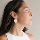 Woman wearing a silver disc earring with a neutral background