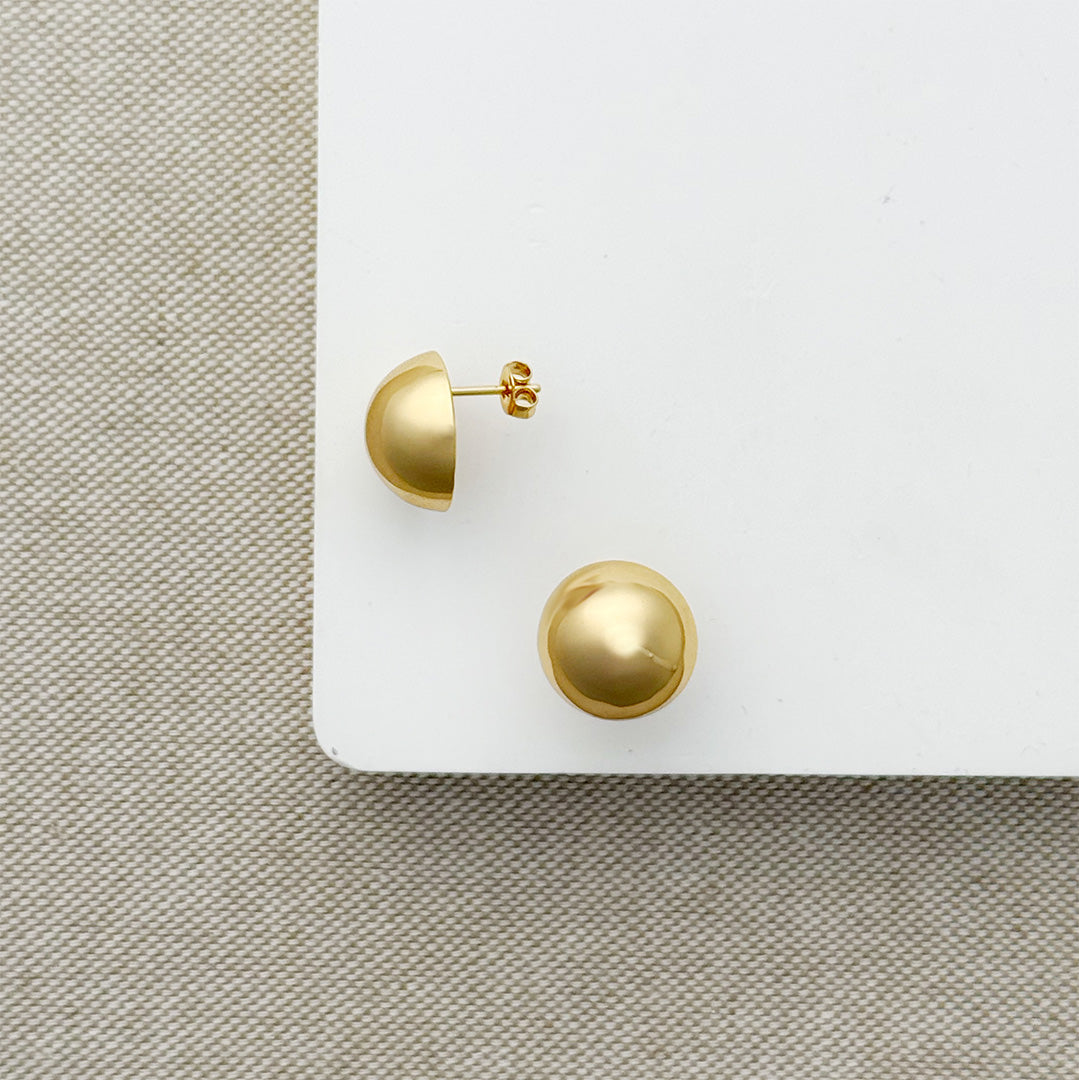 Gold dome earrings on a white surface with a textured beige background