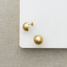 Gold dome earrings on a white surface with a textured beige background