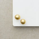 Gold dome earrings on a white surface with a textured beige background
