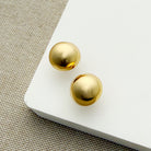 Gold dome earrings on a white surface with a textured beige background