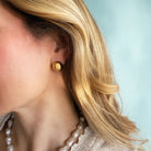 Close-up of a person wearing a large gold dome earring with a light blue background